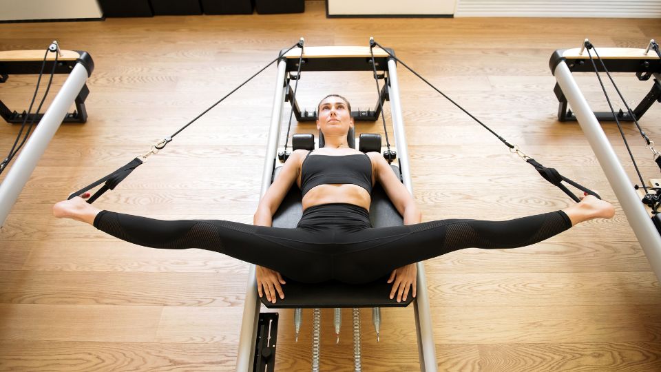 Egy nő csípőnyitó gyakorlatot végez egy pilates gépen, lábait szétnyitva tartja.