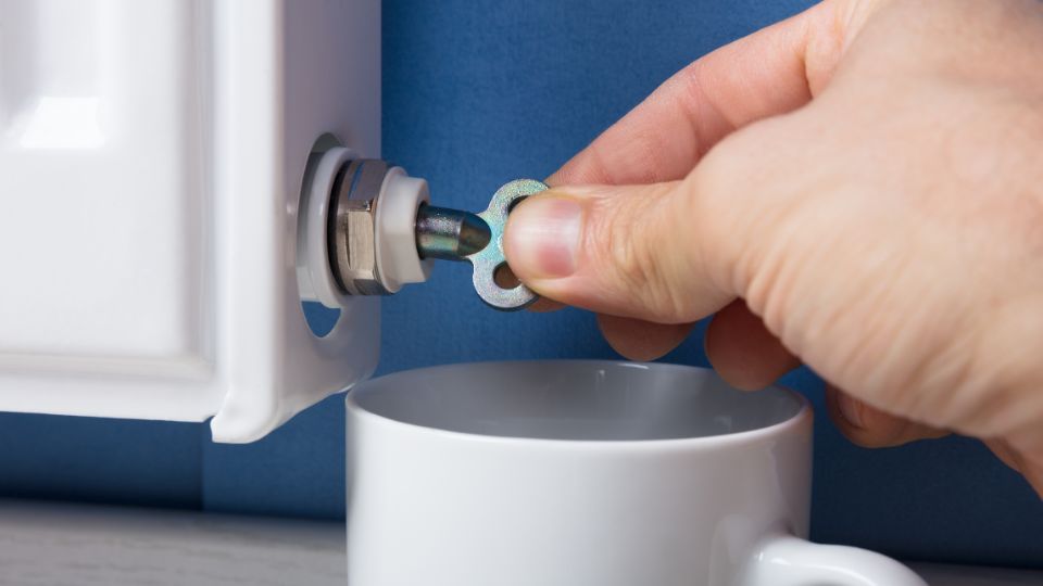 Egy kéz radiátorszelepet állít be, miközben egy csésze alatt áll.