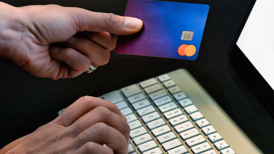 Egy kéz egy Revolut bankkártyát tart, miközben egy számítógép billentyűzetén gépel.