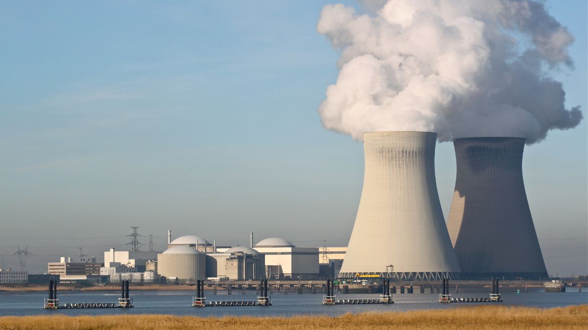 Két hűtőtornyú gőzt bocsát ki egy atomerőmű mellett, vízparti látképpel.