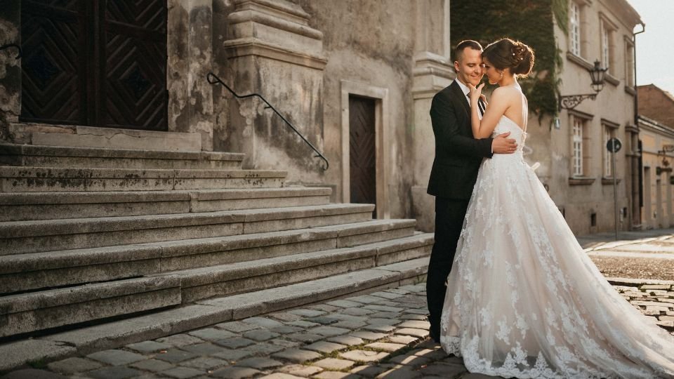 Egy fiatal pár ölelkezik egy templom lépcsőjén, esküvői ruhában.